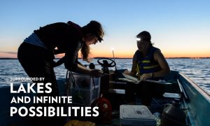 Photo of two students taking lake samples from a boat on Lake Mendota with caption 