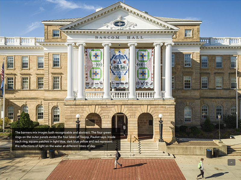 A screenshot from the Seed by Seed website showing the front of Bascom Hall with the three panels of the Seed by Seed banner hanging between tall, white columns above the building's main entrance. The banners contain symbols and colors representing traditions of the Ho-Chunk Nation.
