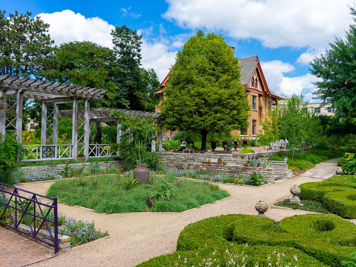 Scenic view of Allen Centennial Garden featuring a pergola, shaped shrubbery, and many varieties of plants and trees.