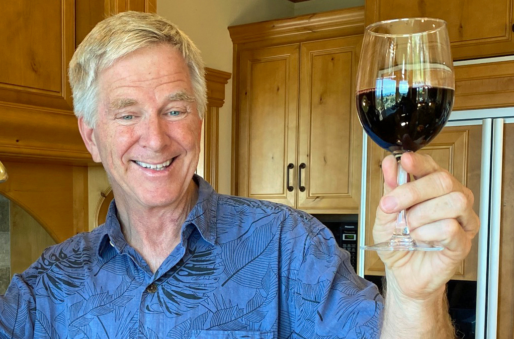 Rick Steves holding a glass of red wine in a kitchen.