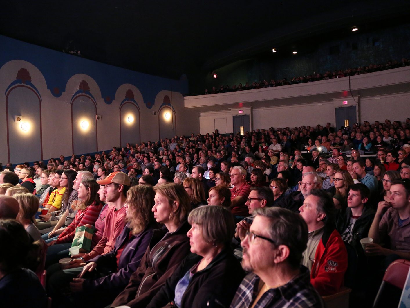 An audience in a full theater intently watches a film.