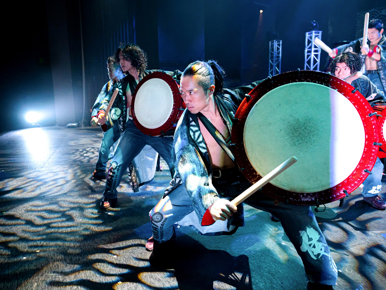 Five members of YAMATO performing with percussion instruments on stage.