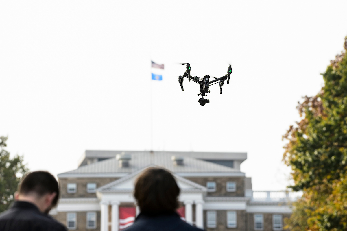 Drone flying overhead controlled by two people in foreground.
