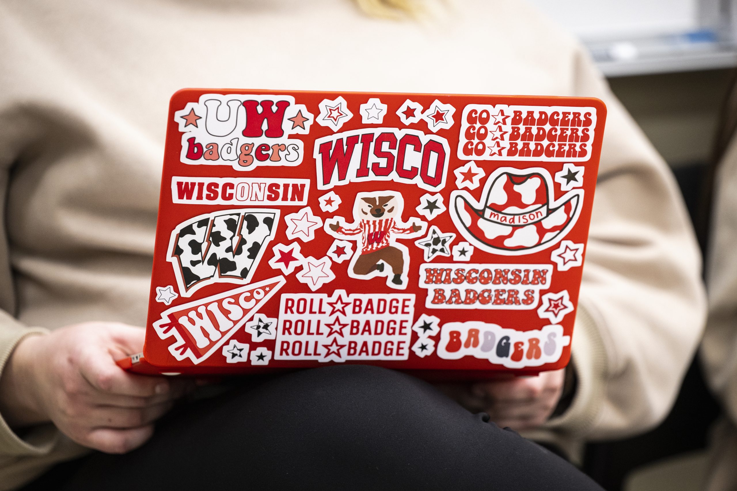 Person working on red laptop decorated with University of Wisconsin–Madison decals.