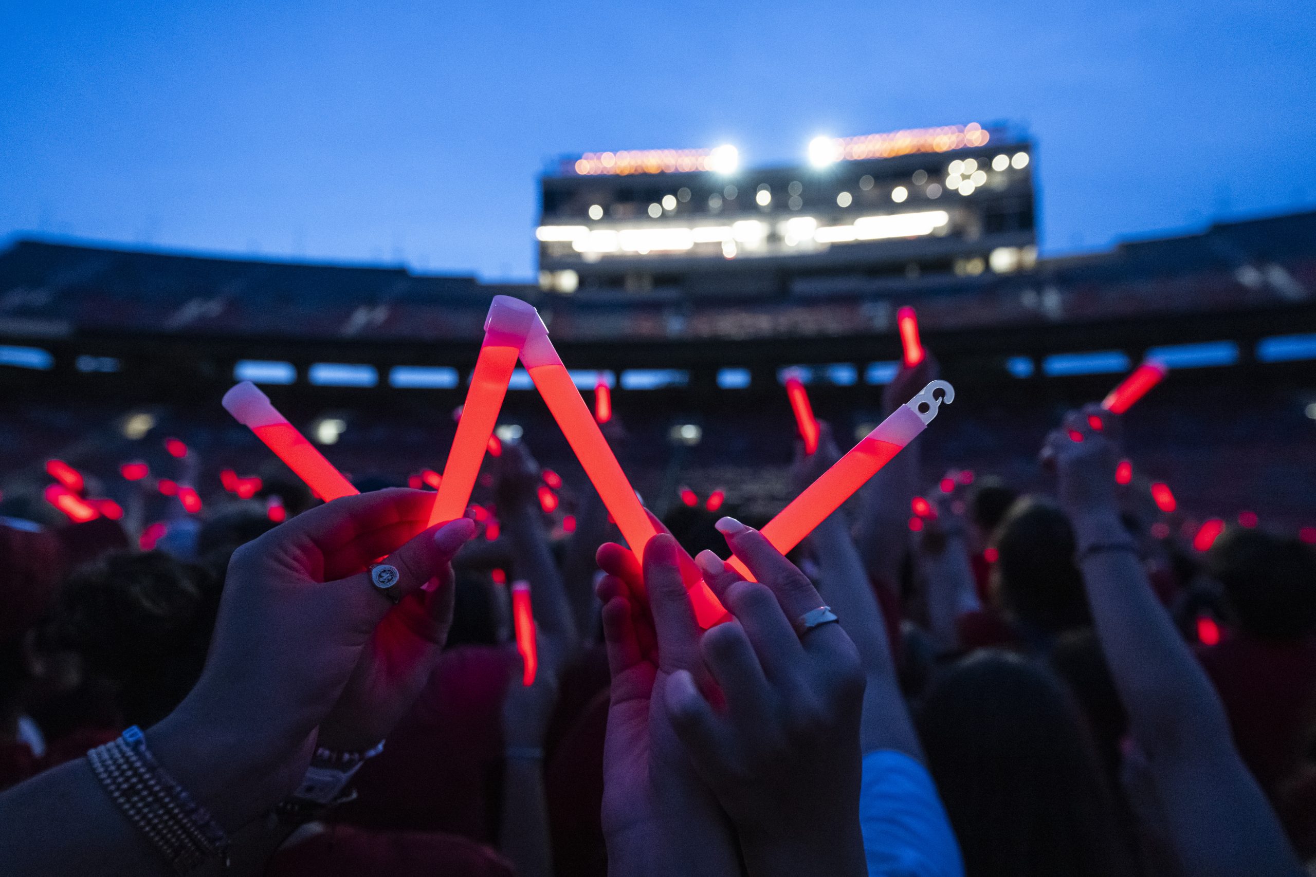 Large crowd of people at night in a stadium holding up red glow sticks in the shape of a W.