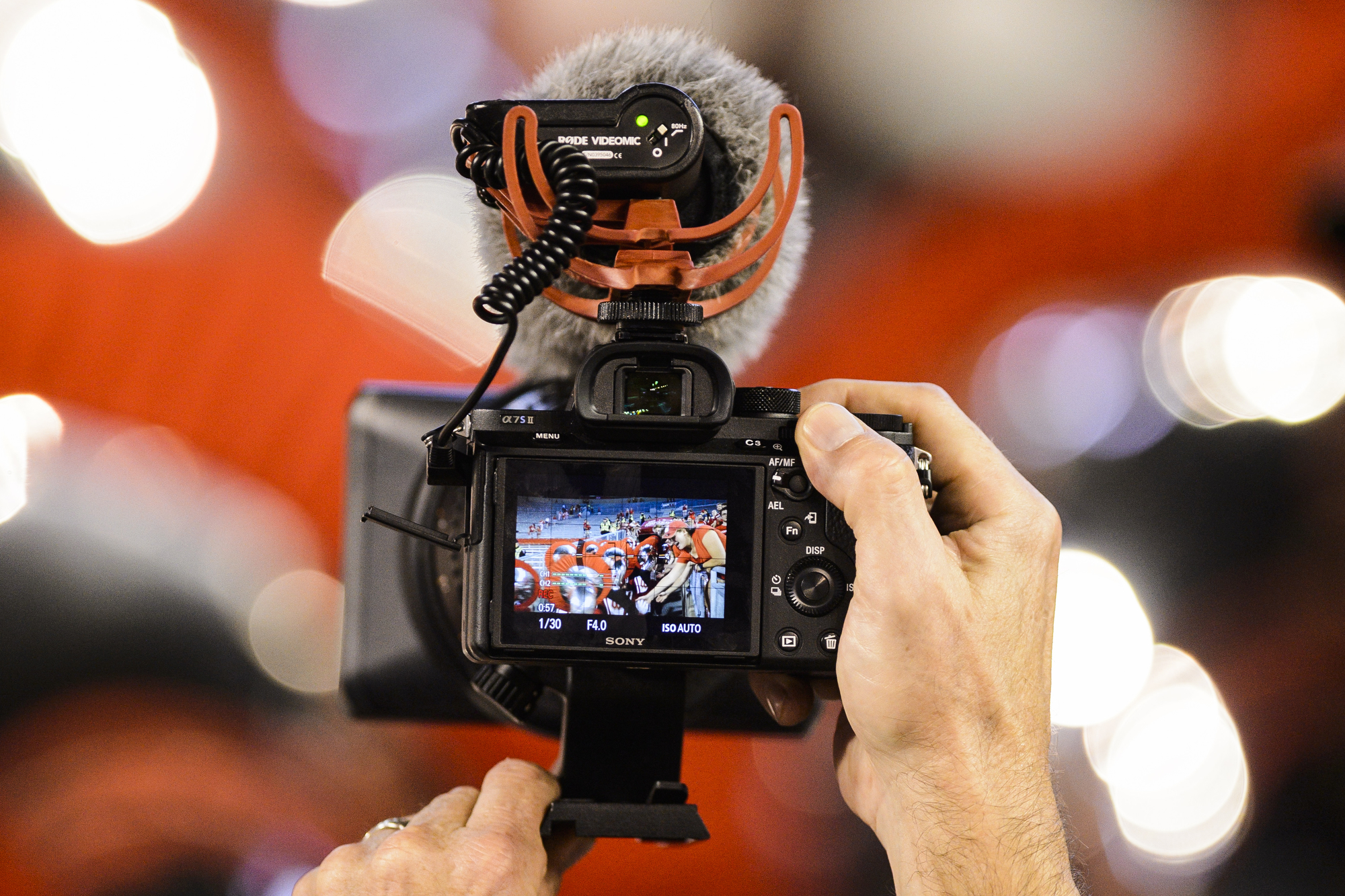 Hand holding a camera facing a blurred red and white background.