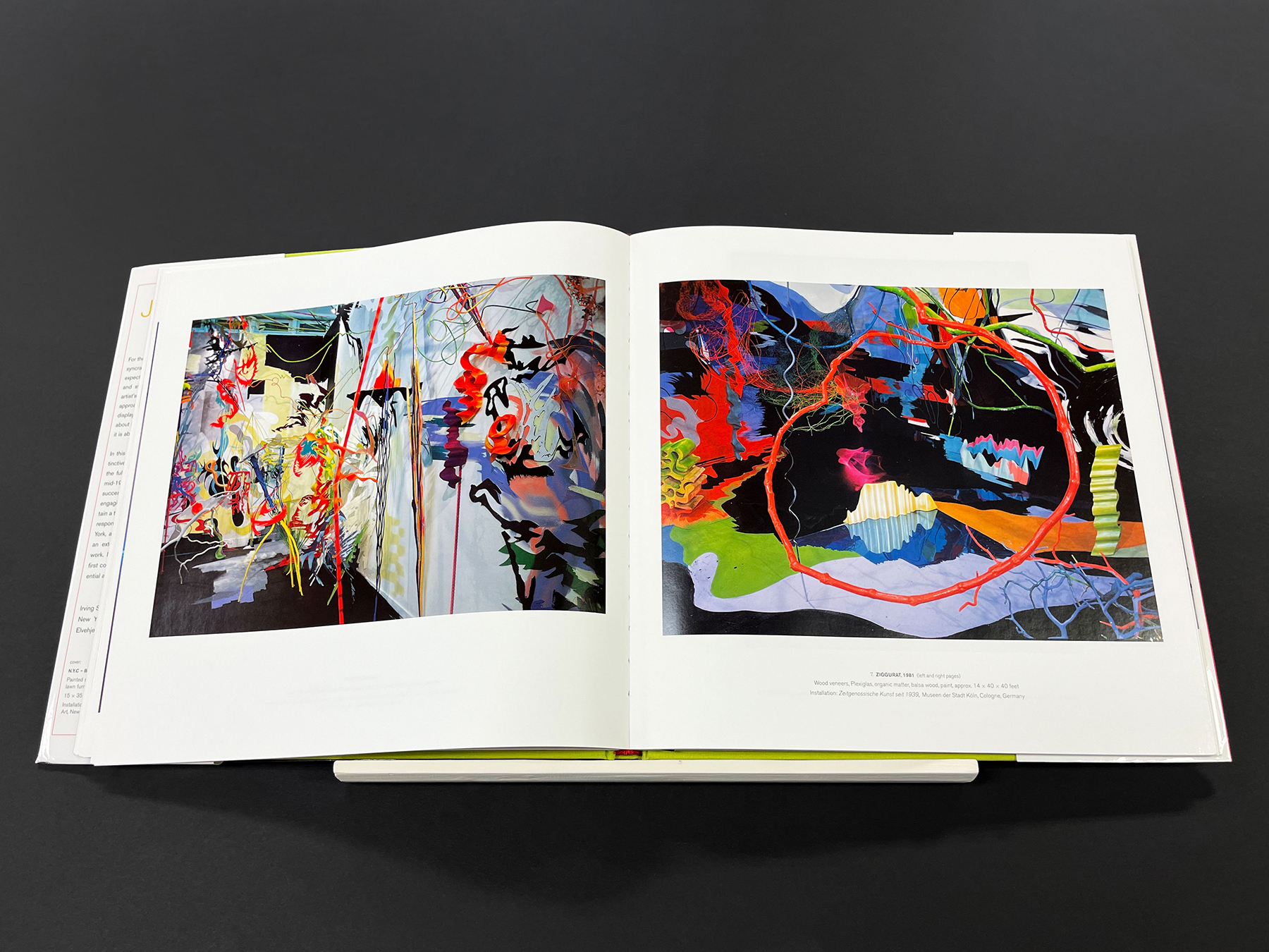 Open art book displaying two colorful abstract artworks with swirling lines, vivid shapes, and layered textures on a black background.