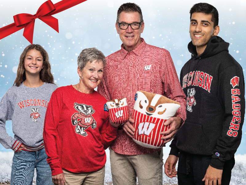 Four people wearing Wisconsin Badgers apparel, including sweatshirts and a button-up shirt, stand together holding plush Bucky Badger items against a snowy background with a red ribbon in the corner.
