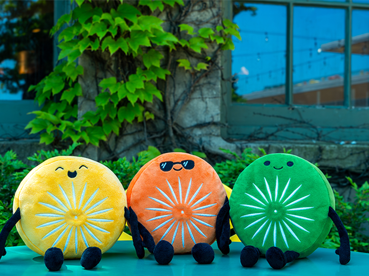 Three Terrace Chairling Plushies -- circular characters with different faces in yellow, orange and green -- sitting on a terrace table outside Memorial Union.