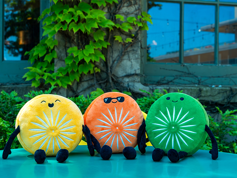 Three Terrace Chairling Plushies -- circular characters with different faces in yellow, orange and green -- sitting on a terrace table outside Memorial Union.