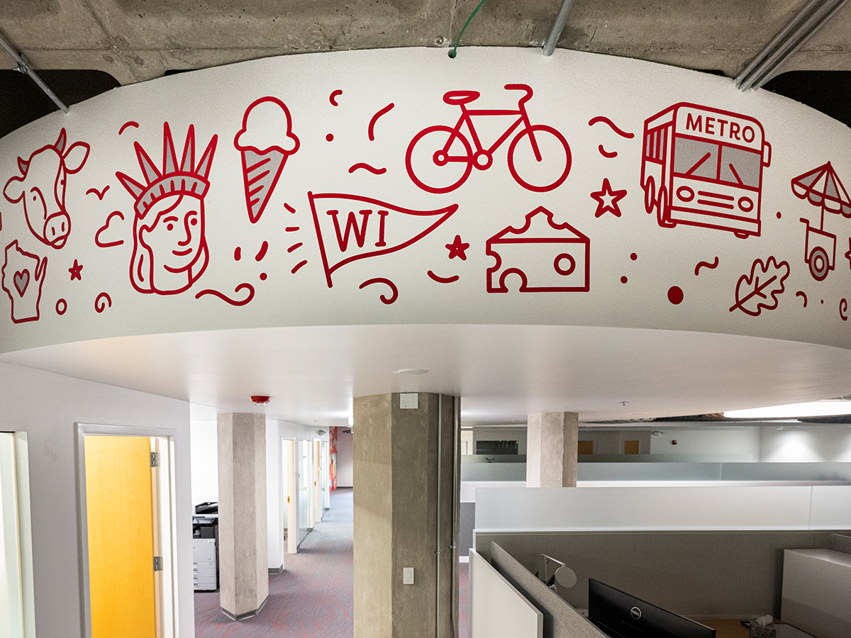 After photo of a circular architectural feature within an office space with red doodles depicting UW–Madison icons such as a cow, a pendant, bicycle, a bus, and a food cart.