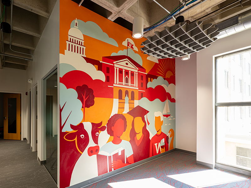 Office interior with a brightly painted mural of buildings, students, and UW–Madison icons.