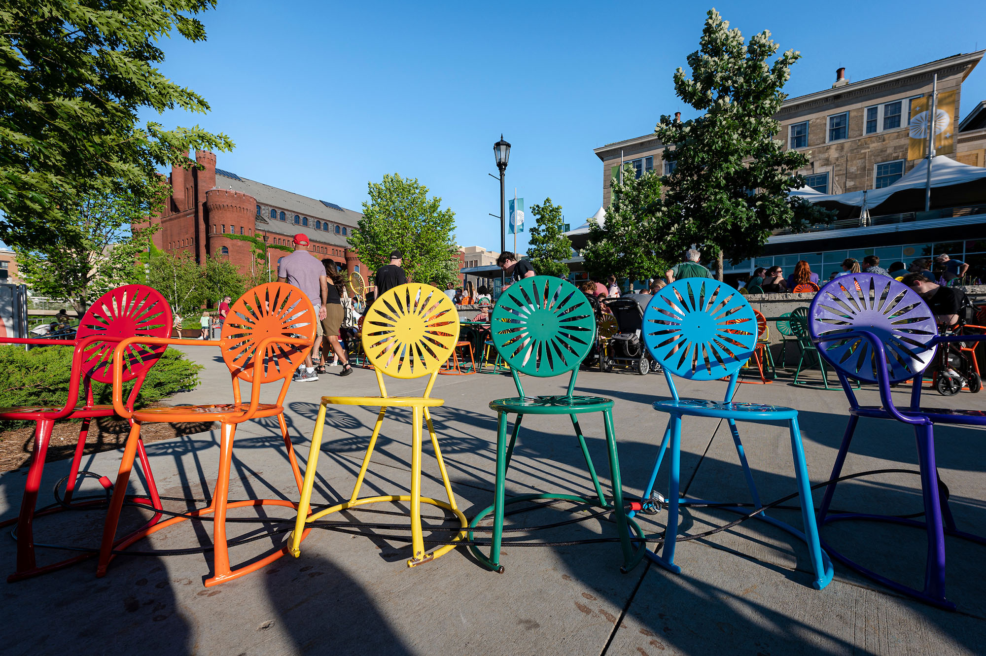 Red, orange, yellow, green, blue and purple union chairs lined up on the Memorial Union Terrace on a summer day.