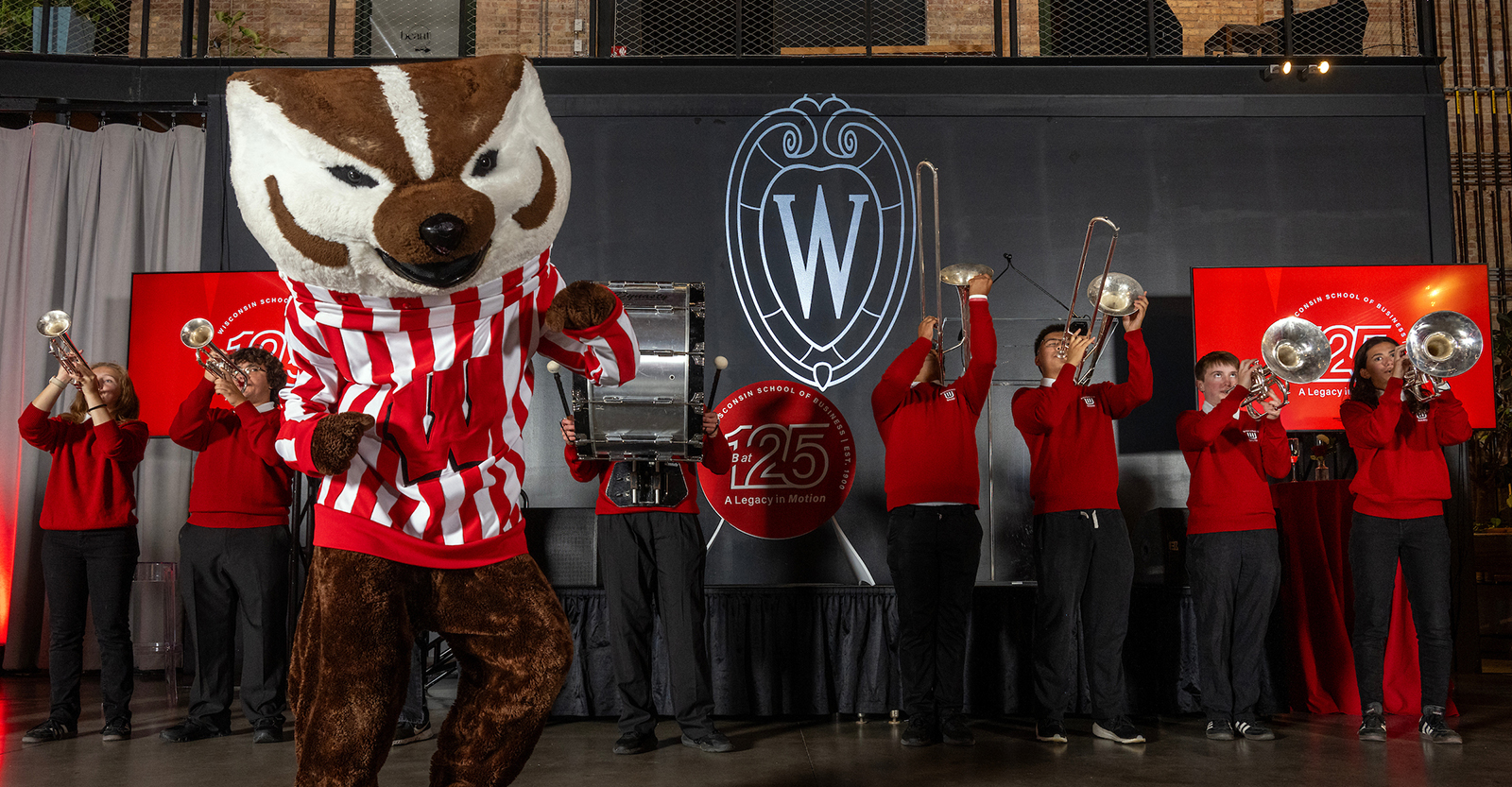 Bucky Badger mascot dancing with members of a band playing instruments in the background