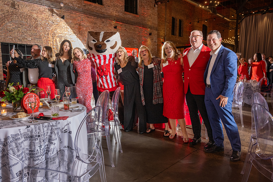 Group of people and Bucky Badger mascot at a gala linking arms while swaying and singing
