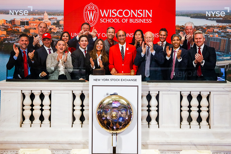 Group of people cheering and clapping in front of the Wisconsin School of Business logo at the New York Stock Exchange's closing bell.