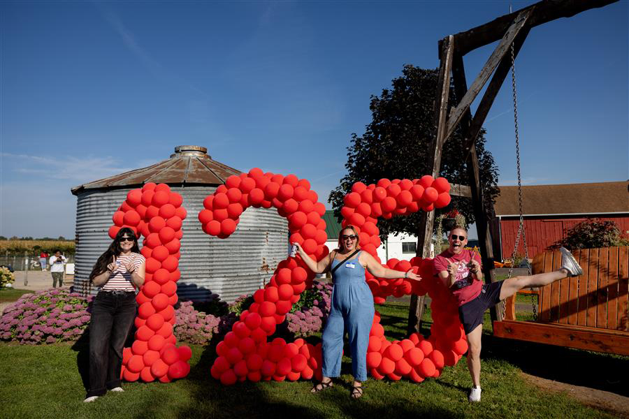 Three people smiling in front of a balloon display of the numbers 125 with a silo and barn in the background.
