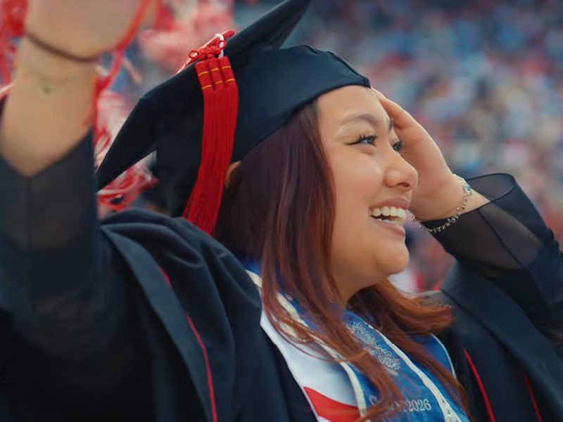 A person in graduation attire, smiling with a raised arm.
